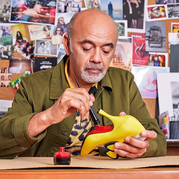 Christian Louboutin aplicando esmalte rojo a la suela de un zapato amarillo