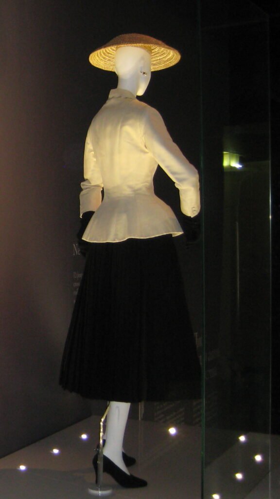 Traje Bar de Christian Dior de la colección Corolle, primavera-verano de 1947, con chaqueta clara entallada, falda negra amplia y sombrero.