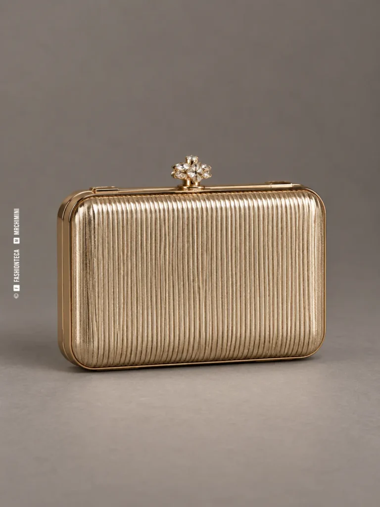 minaudière metálica color champán fotografiada en estudio sobre fondo gris, con cuerpo acanalado, bisagra y cierre decorativo
