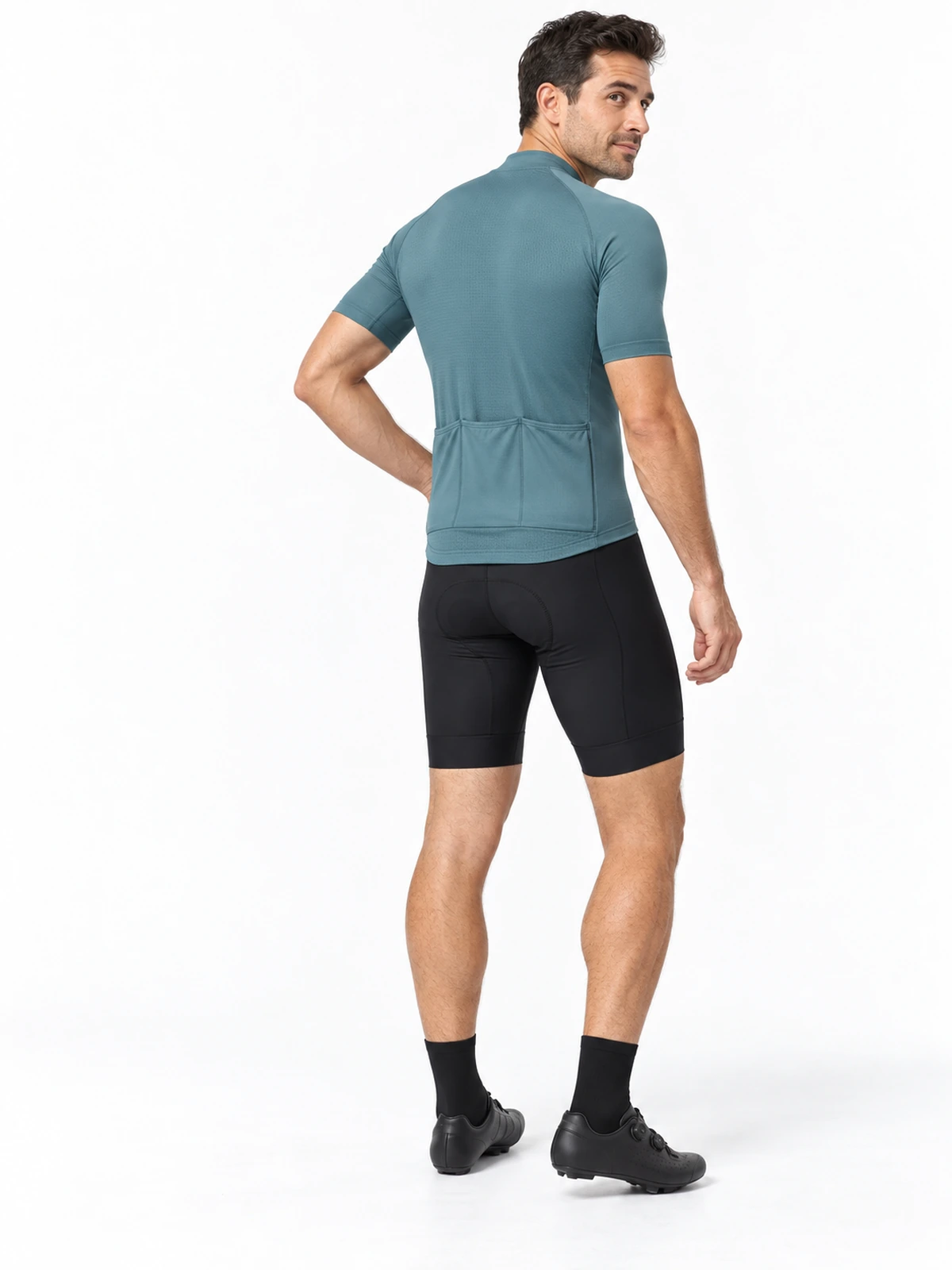 Ciclista adulto visto de tres cuartos de espalda con maillot verde azulado, mangas cortas y tres bolsillos posteriores, sobre fondo blanco.