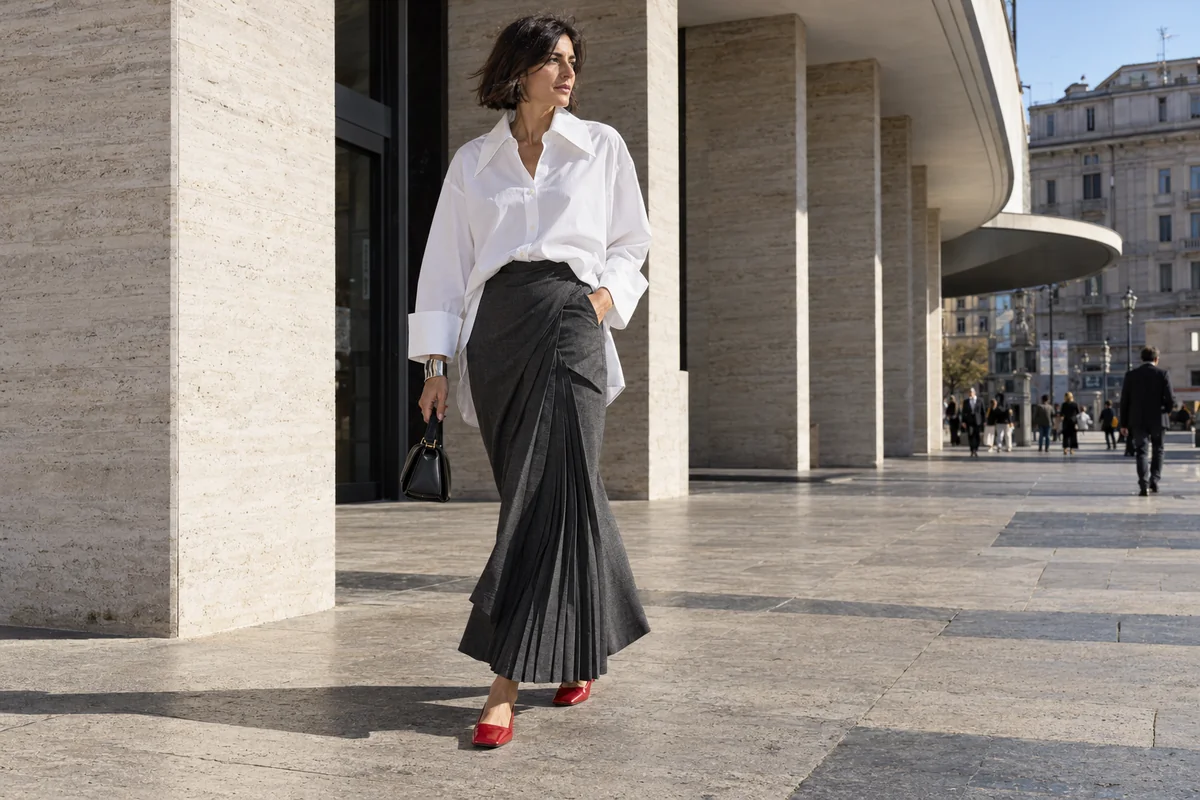 Camisa blanca de mangas amplias y puños largos combinada con falda oscura asimétrica y zapatos rojos.