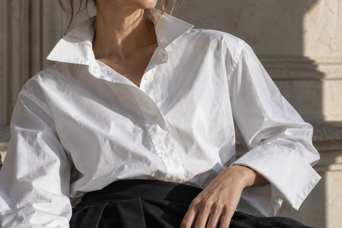Detalle del cuello, botonadura y puño amplio de una camisa blanca con pliegues y costuras visibles.